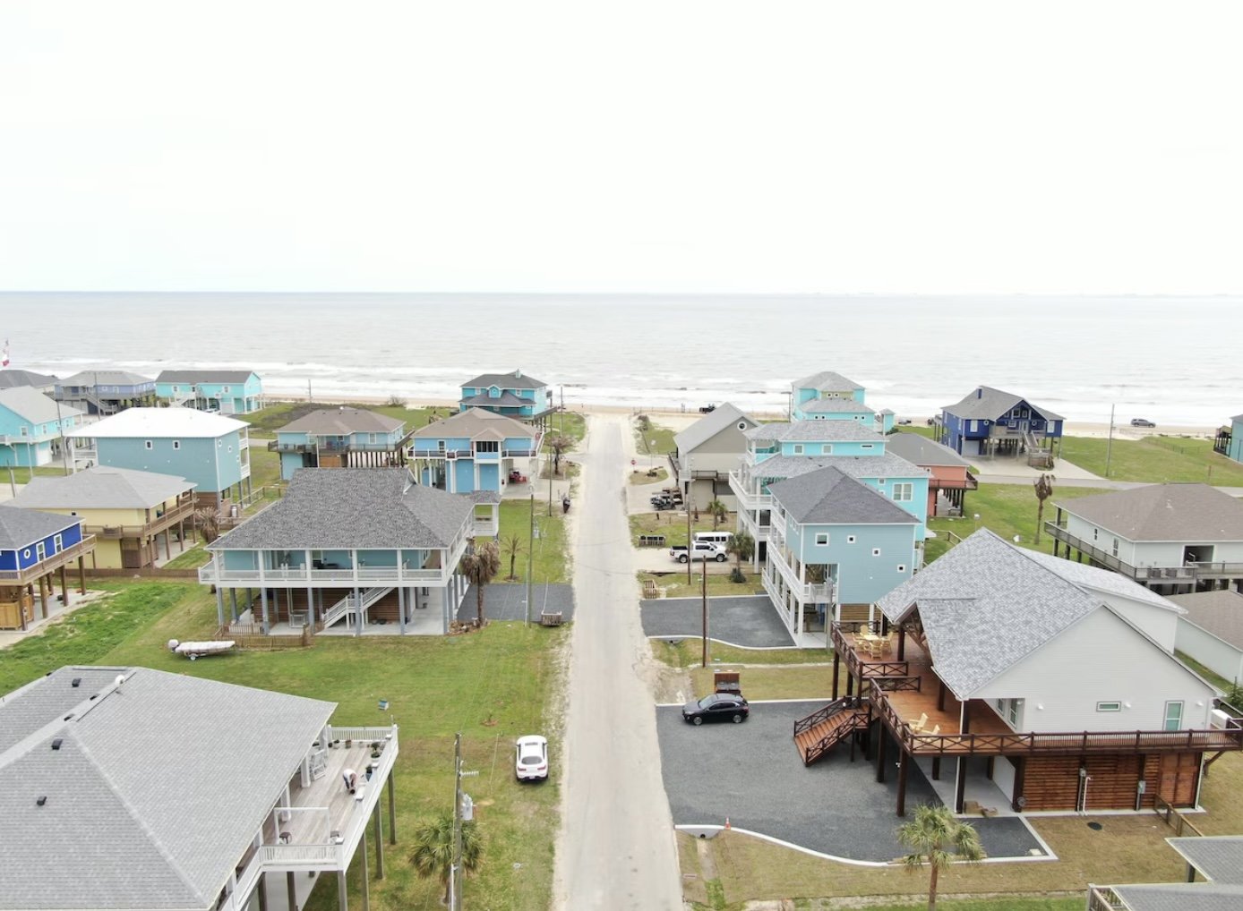 Overhead view of a coastal neighborhood with colorful beach houses and a sandy beach in the background overlooking the ocean.