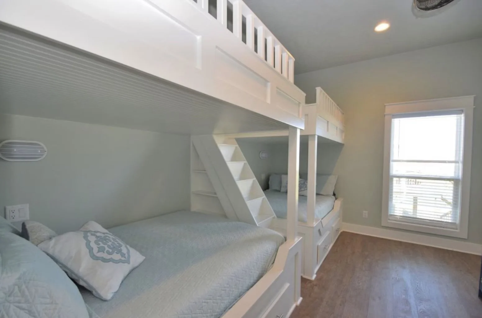 Bedroom with bunk beds, a window with blinds, and hardwood flooring.