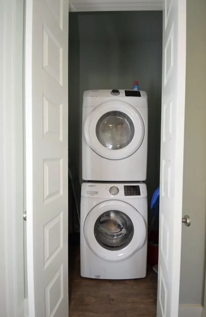 A washer and dryer stacked vertically inside a small closet with double doors open.