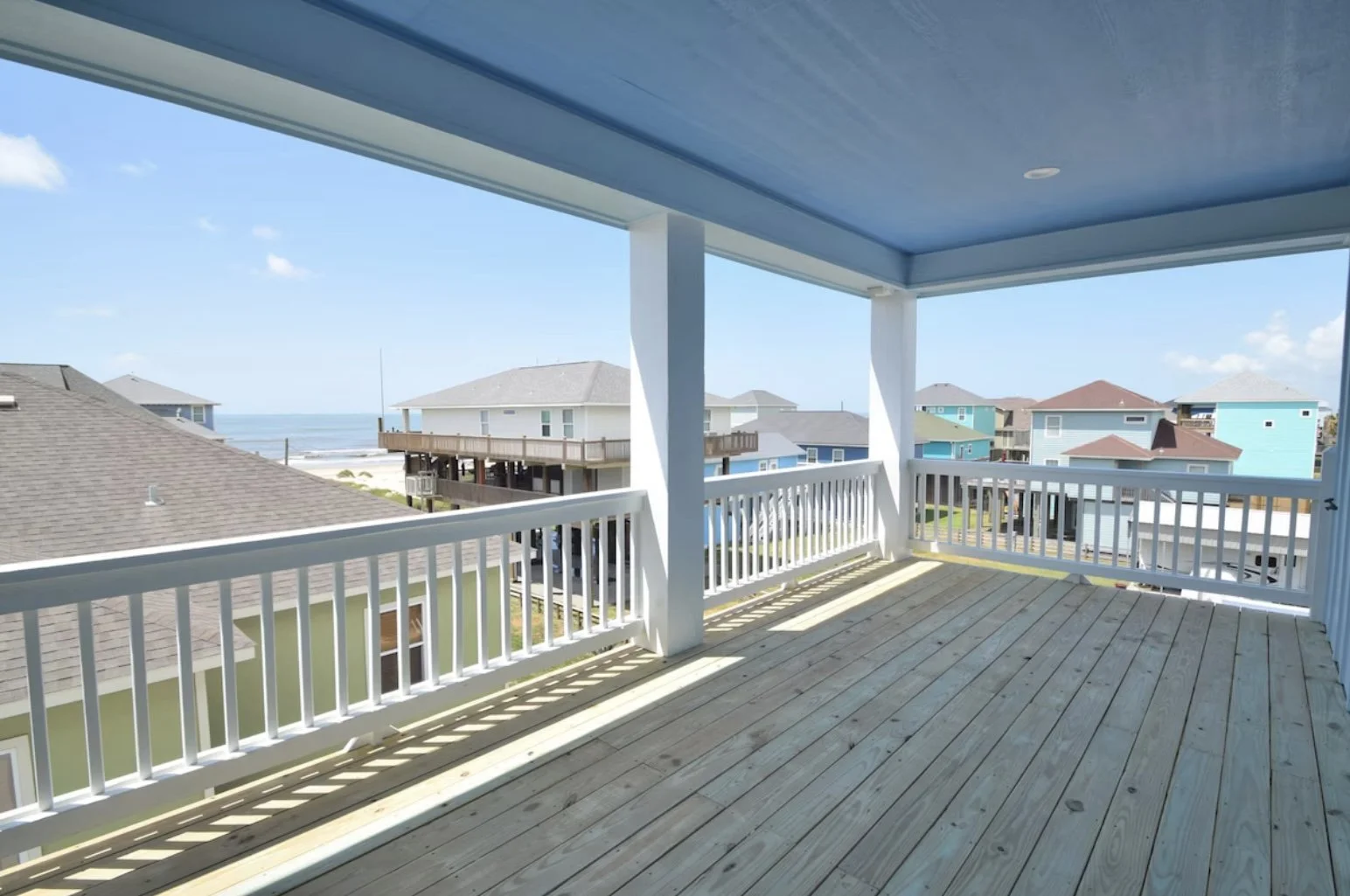 View from a balcony overlooking a neighborhood of beach houses with the ocean in the background on a clear, sunny day.