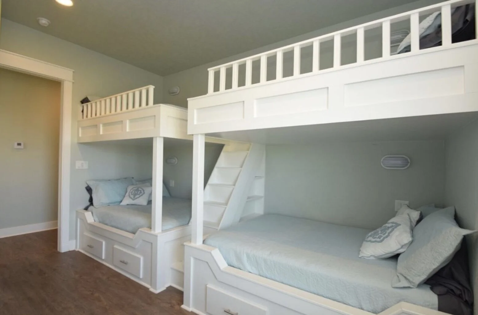 Room with built-in bunk beds with stairs, surrounded by light green walls and hardwood flooring.