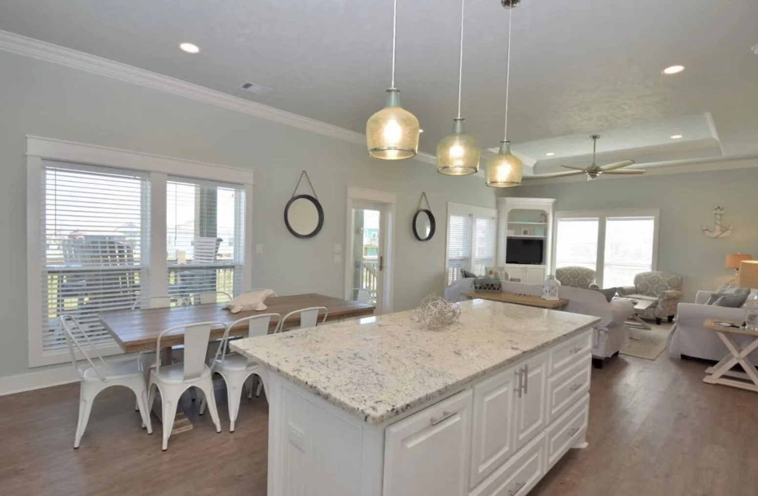 Open-concept living room and kitchen with island, pendant lights, dining table, and seating area with couches and windows