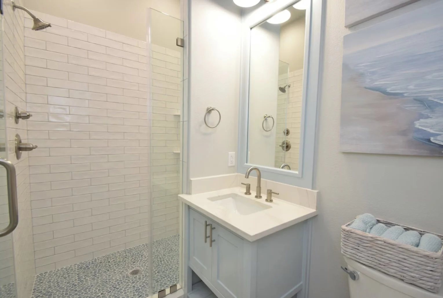 Bathroom with glass shower enclosure, white brick tiles, vanity with a mirror, and a basket of rolled towels.