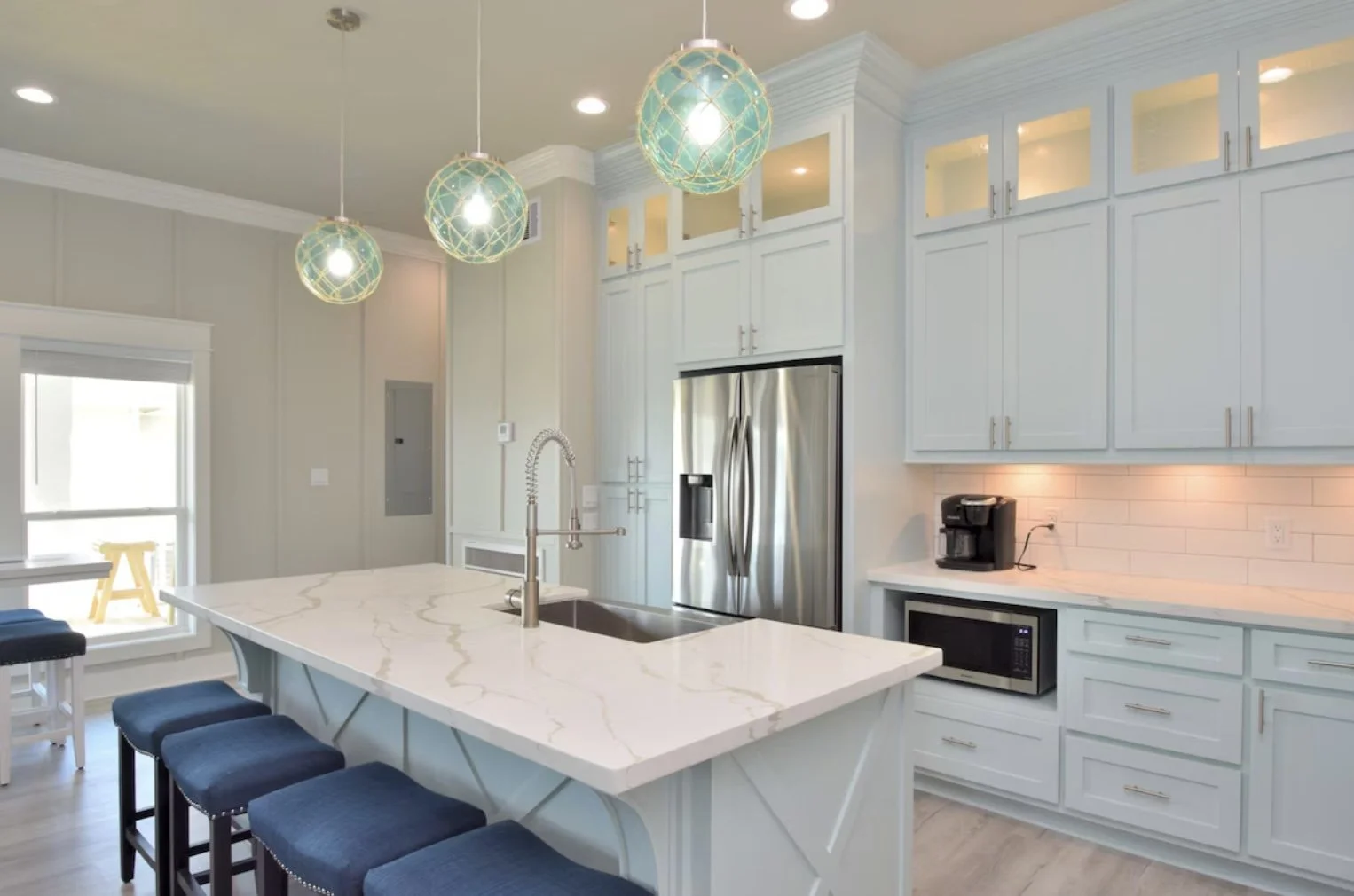 Modern kitchen with white cabinets, stainless steel refrigerator, marble island with blue barstools, and pendant lighting