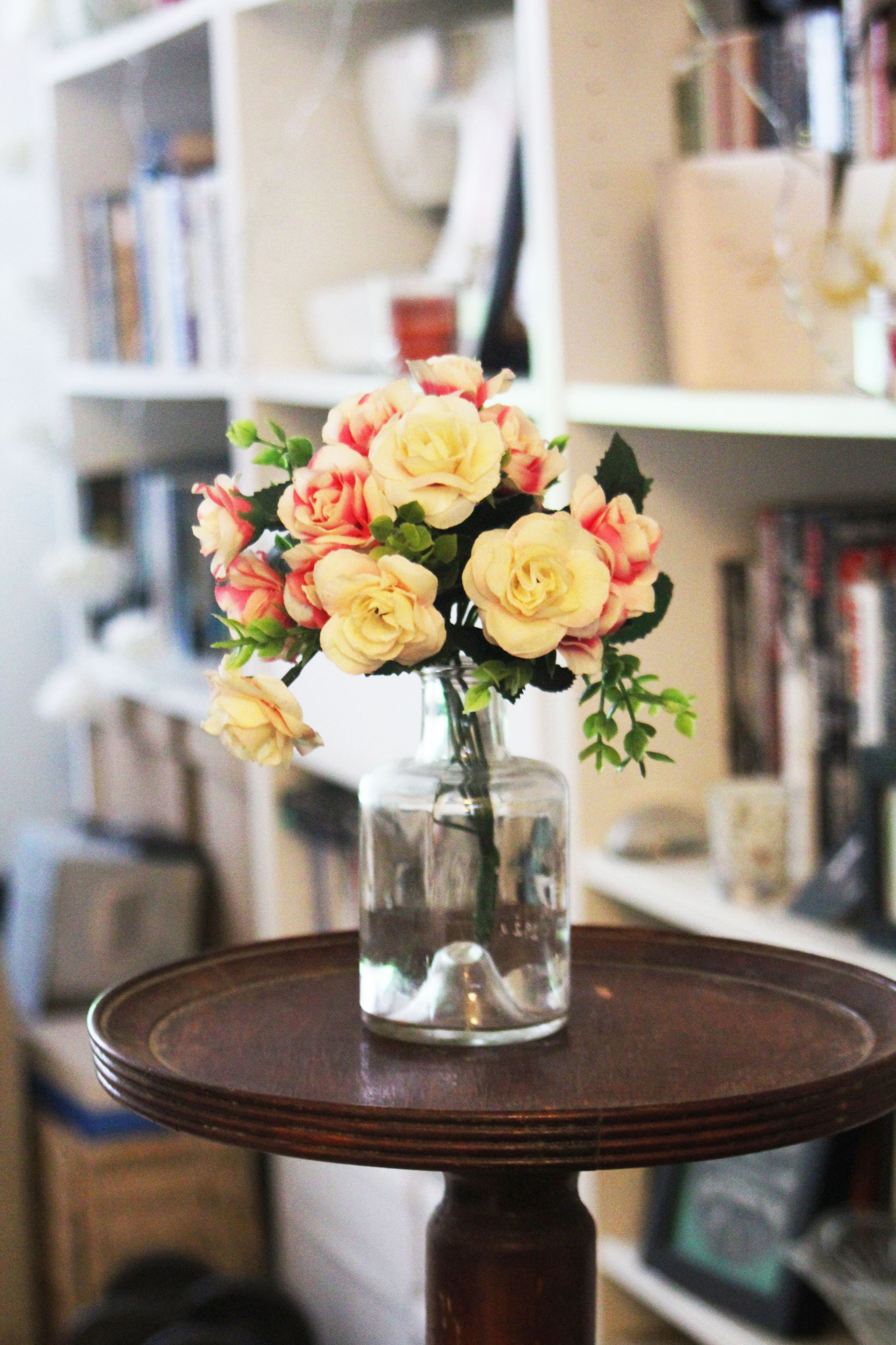 A flower bouquet is placed on a wooden table with a backdrop of a library of books and other paper materials.