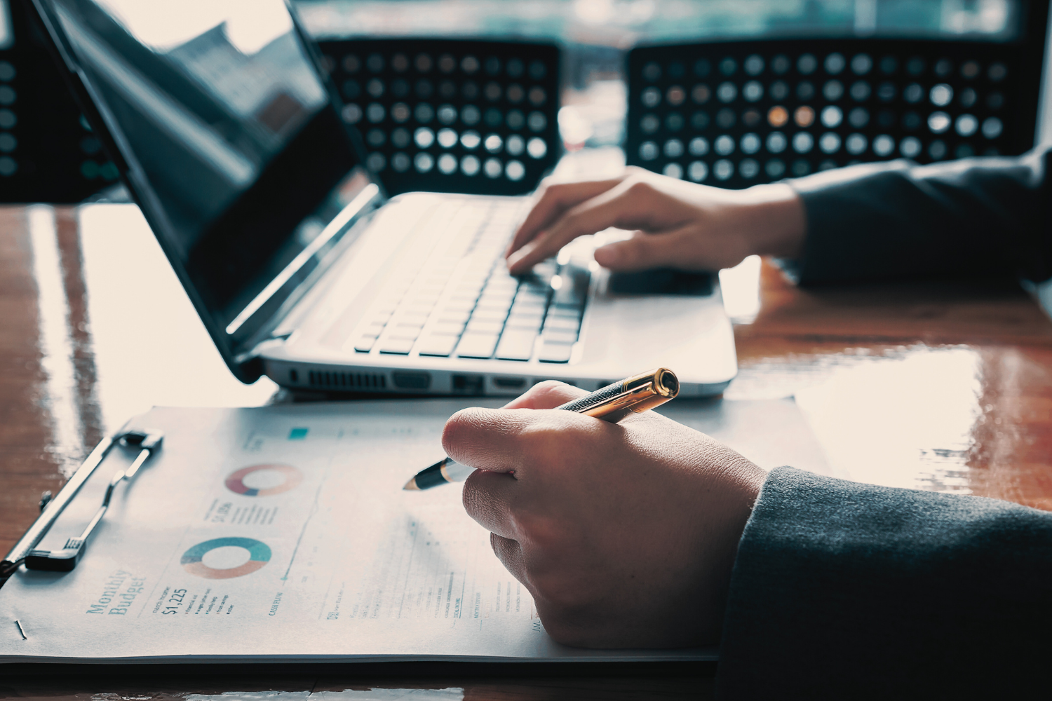 Person working with a laptop and financial documents on a wooden table.
