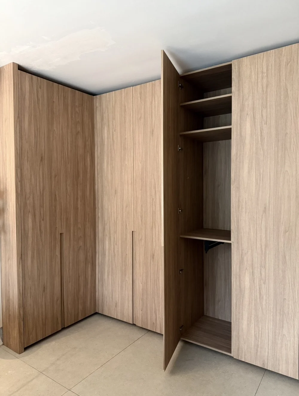 Full-height woodgrain custom wardrobe wrapping a corner in Miami Beach, with one door open to show fitted shelves