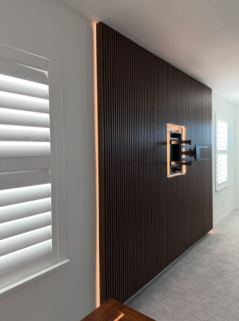 Vertical slat wall with an exposed television bracket and warm lighting along the outer edge