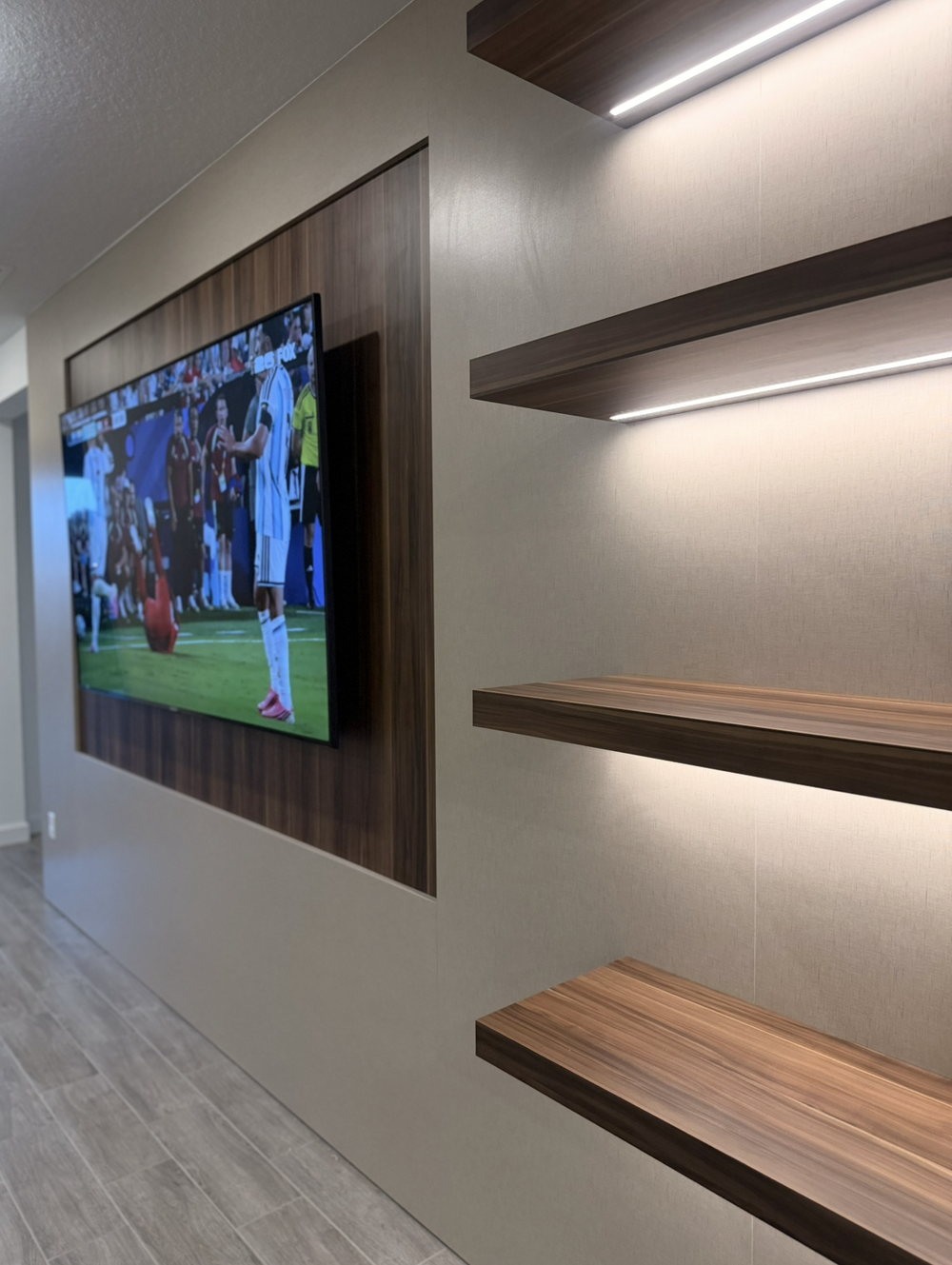 Angled close view of illuminated woodgrain floating shelves, a vertical side return and a television back panel