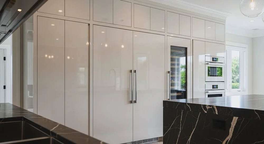 Glossy white full-height kitchen cabinetry with tall appliance panels, a glazed appliance door, stacked ovens and upper storage
