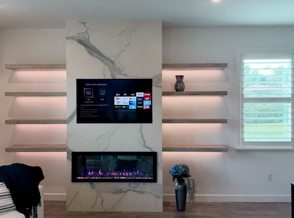 Media wall with a marble-look television and fireplace surround and illuminated floating shelves on both sides