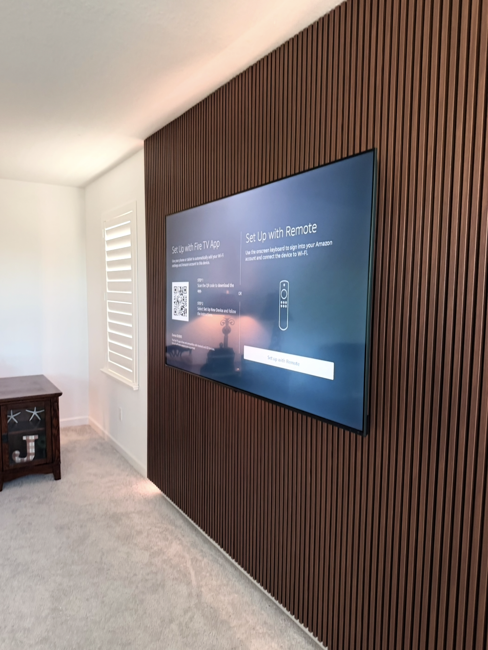 Television mounted on a dark woodgrain vertical slat feature wall between shuttered windows