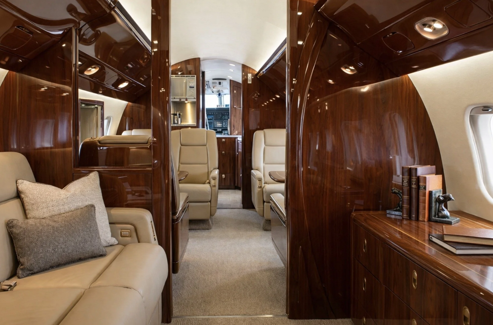 Aircraft cabin with high-gloss brown woodgrain cabinetry, wall panels and overhead trim around cream-colored seating