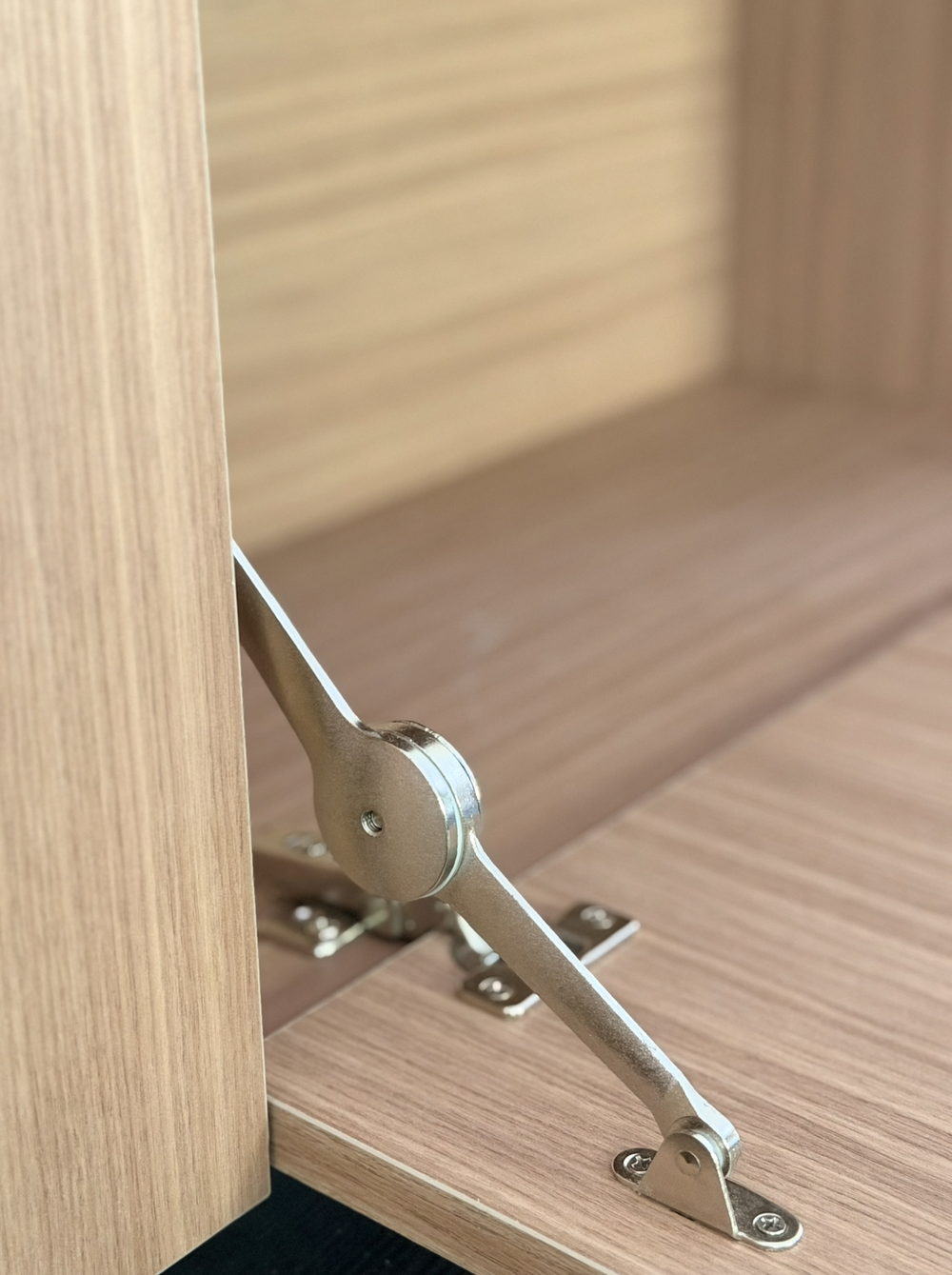 Close view of a metal support mechanism on an open woodgrain drop-down cabinet door