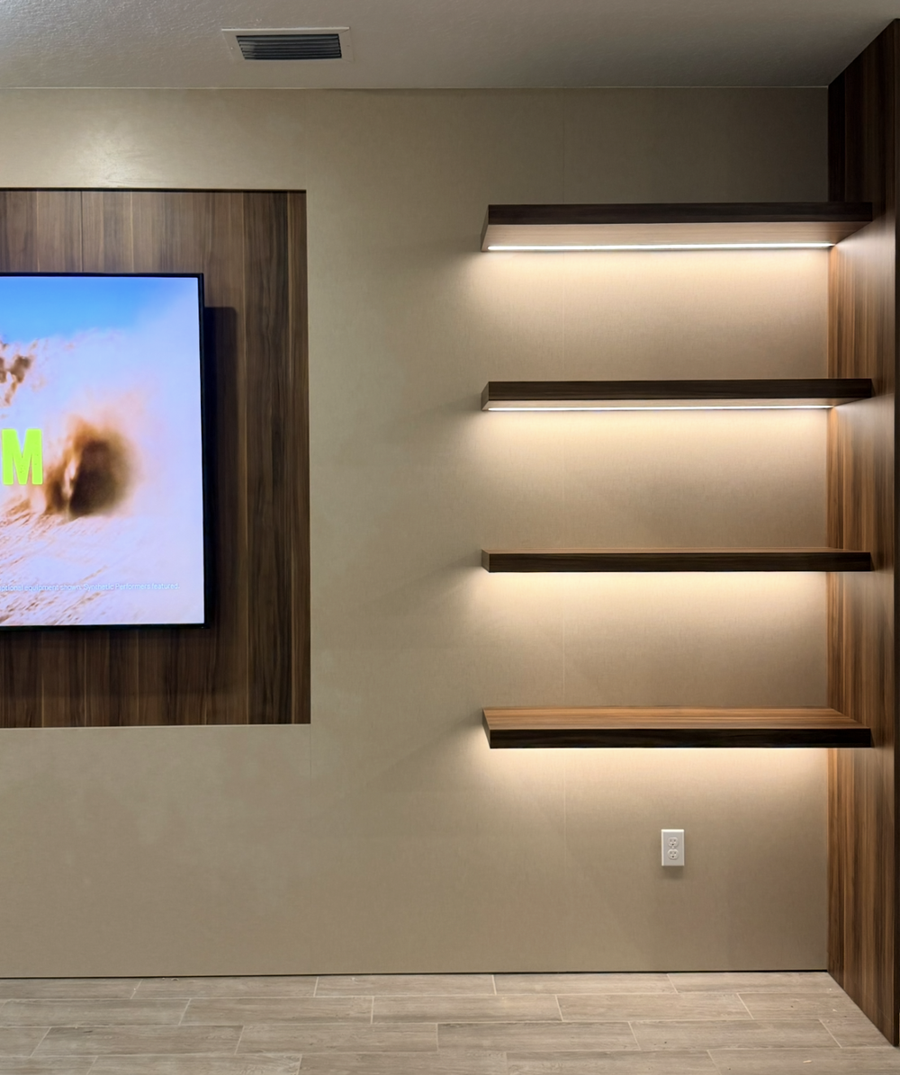 Four woodgrain floating shelves with lighting underneath, beside a matching television back panel