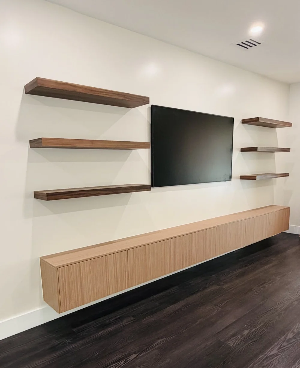 Long floating woodgrain media console beneath a television with three darker floating shelves on each side