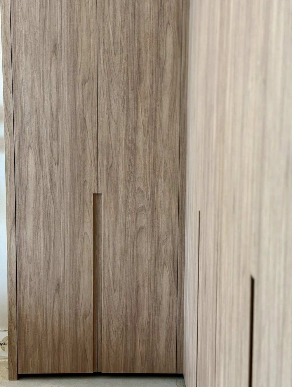 Close view of full-height woodgrain wardrobe doors and recessed pulls in a Miami Beach installation