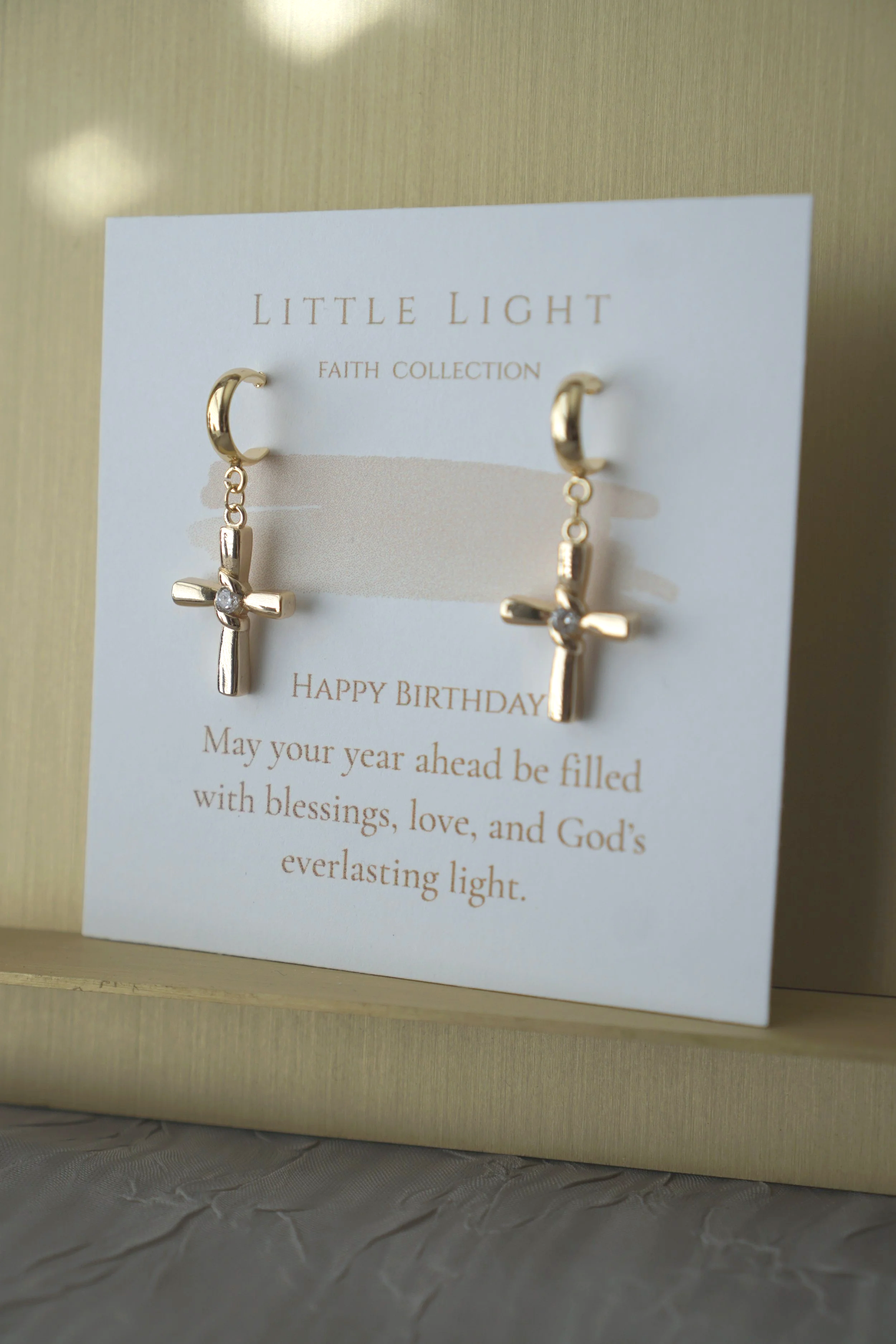Gold hoop earrings with cross charms on a faith-themed birthday card.