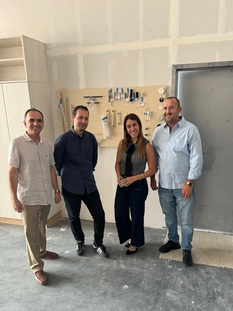 Four people standing inside a room with a project display on the wall and unfinished walls and floor.