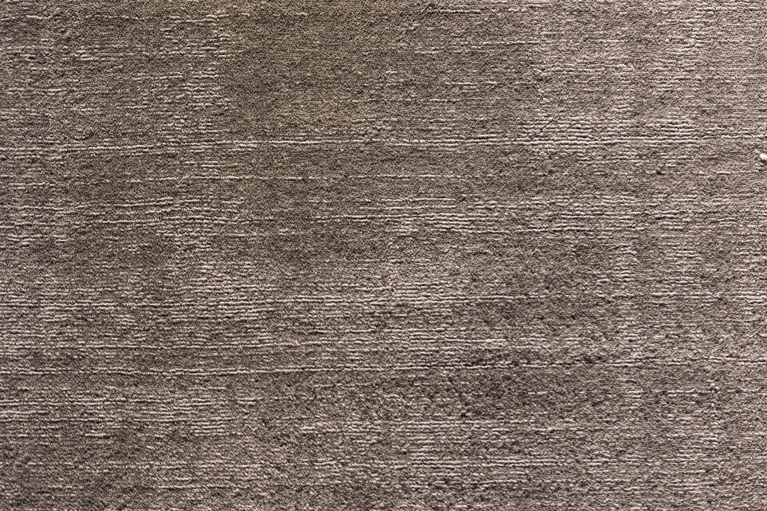Close-up of a textured brown surface, possibly a carpet or fabric, with horizontal lines and a slightly rough pattern.