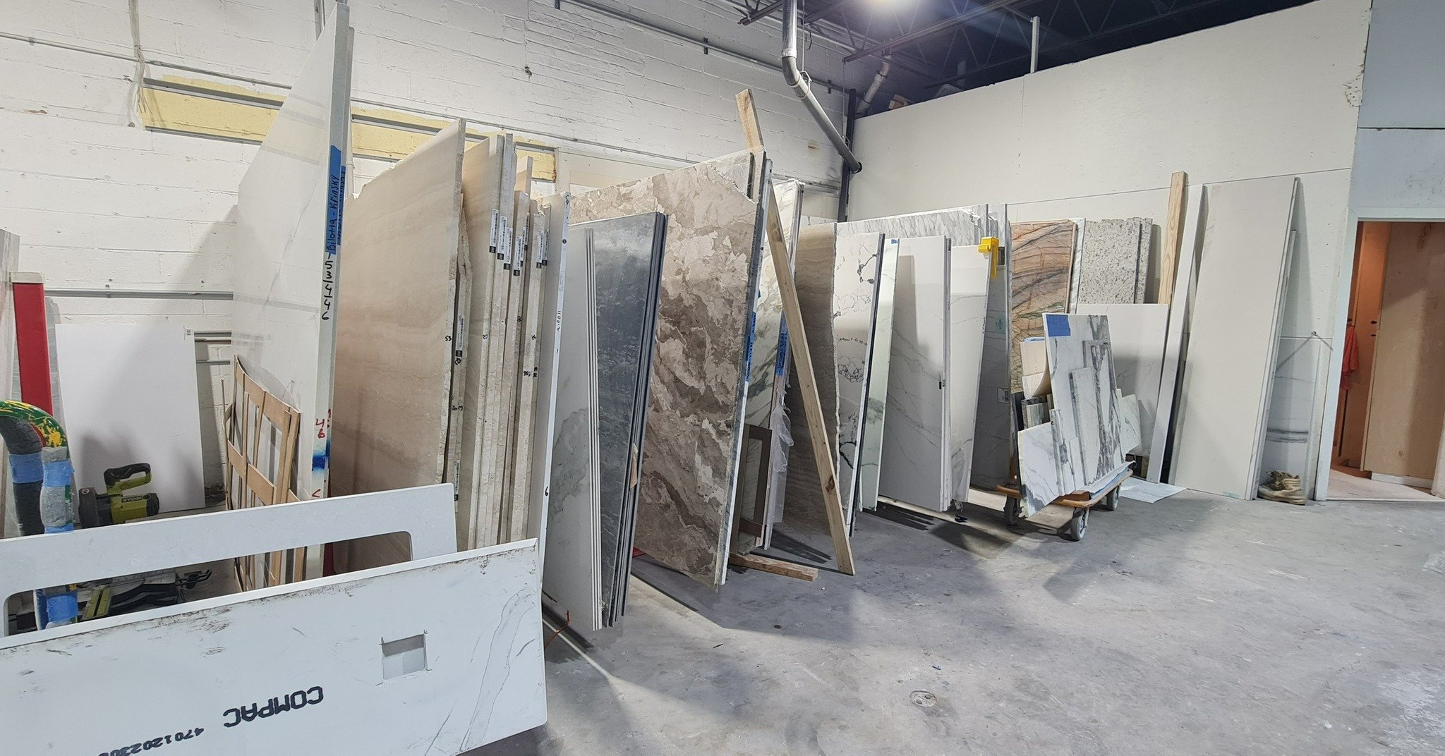 A warehouse or showroom with large slabs of marble and stone leaning against racks and walls, with some construction tools visible.