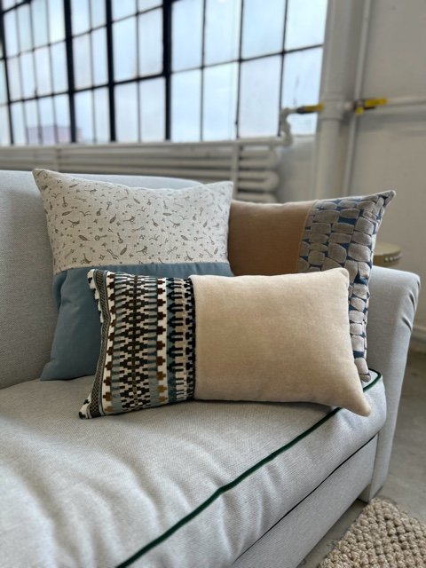 Four decorative pillows on a light gray couch in front of a large window with a white radiator underneath.
