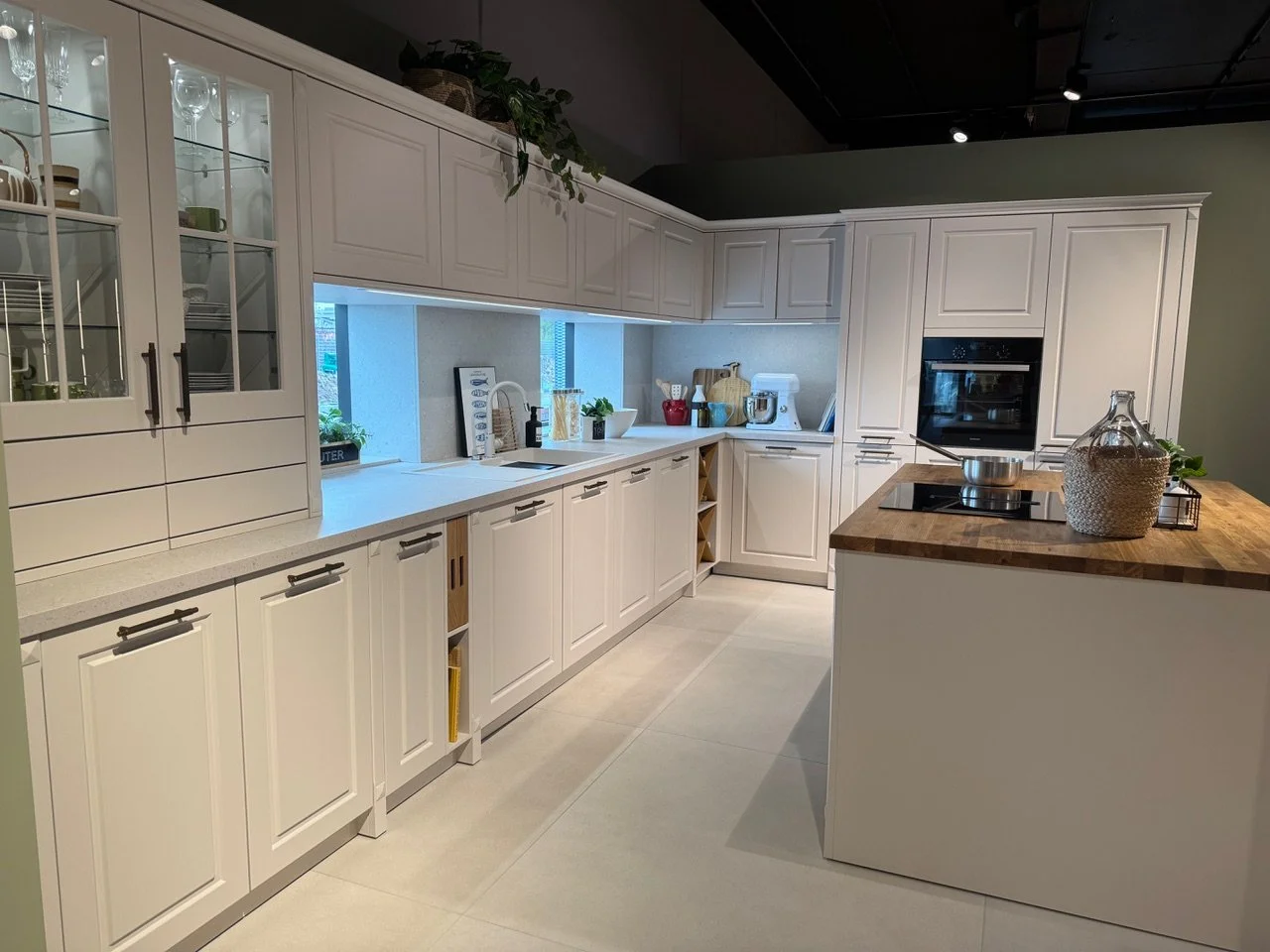 Modern kitchen with white cabinets, a wooden island, and a window with plants.