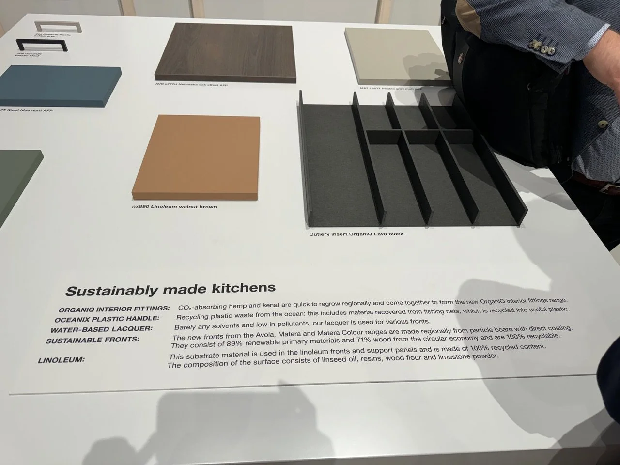 Display table showing various material samples for sustainable kitchen design, including color swatches and sample panels labeled with material names.