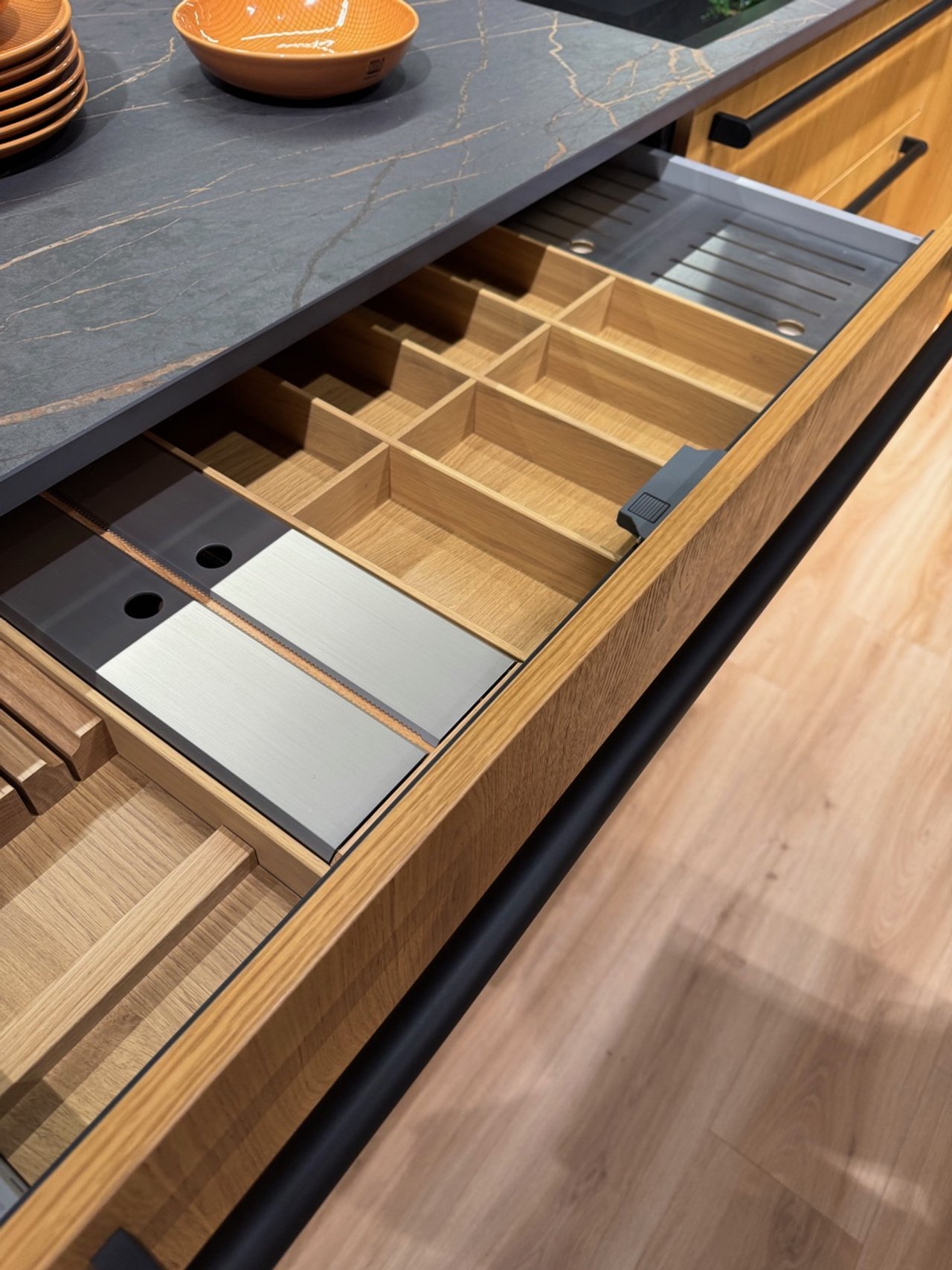 Open kitchen drawer with empty wooden compartments and metal sections for utensils or accessories.