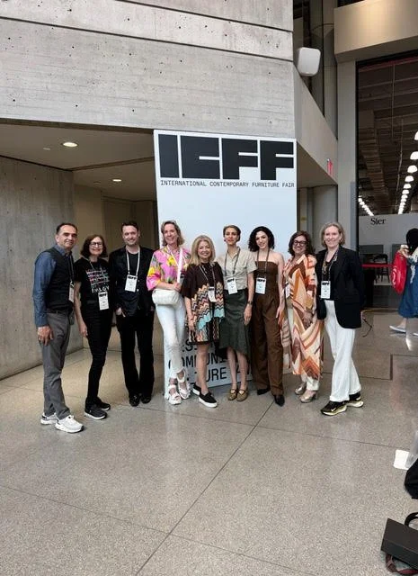 A group of nine people posing in front of a sign that reads 'IFIFF International Contemporary Furniture Fair' at an indoor event.