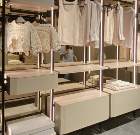 Clothing store display with white and beige sweaters and shirts on hangers and shelves.