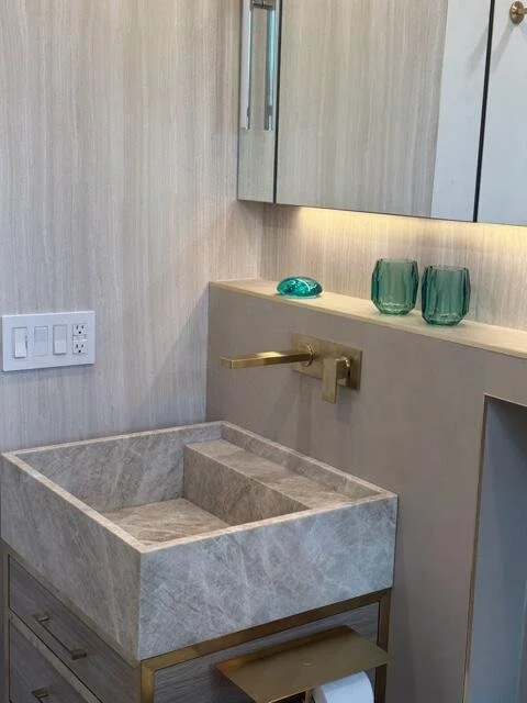 Bathroom with marble sink, gold faucet, a mirror, and decorative glass objects on the countertop