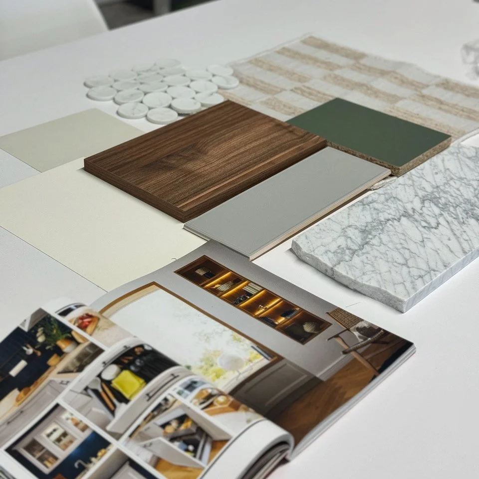 Samples of interior design materials including wood, tile, marble, fabric swatches, and a home decor magazine on a white table.