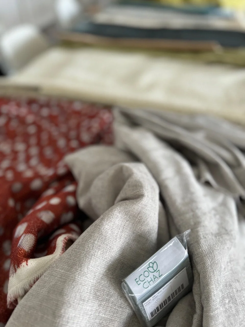 Close-up of a pile of fabric swatches, including patterned and plain cloth, with a transparent box labeled EcogChaz with a barcode.