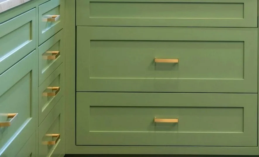Close-up of green kitchen cabinets with gold handles.