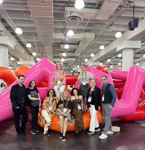 Group of eight people posing in front of large pink and orange inflatable slide inside a convention center.