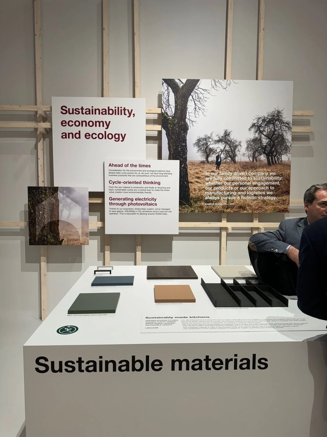 Exhibit display with signs about sustainability, economy, and ecology, including images of trees and text emphasizing sustainability in manufacturing and logistics, with various material samples on a table labeled 'Sustainable materials.'
