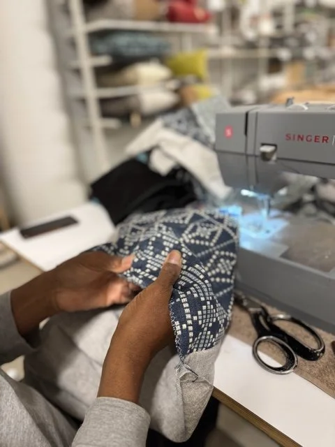 Person sewing blue patterned fabric on a sewing machine in a workspace.