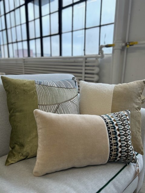 Four decorative throw pillows on a light-colored surface near large industrial-style windows.