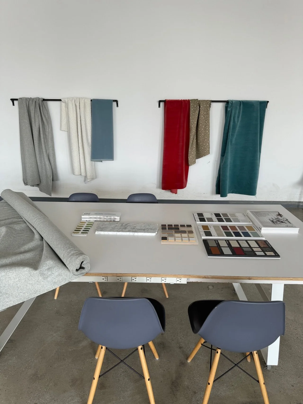A conference room with fabric samples and color swatches on the table in front of two chairs, with fabric samples hanging on the wall in the background.