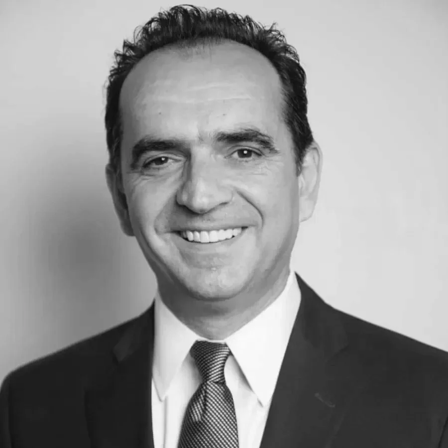 Black and white professional headshot of a smiling man in a suit and tie, facing forward.
