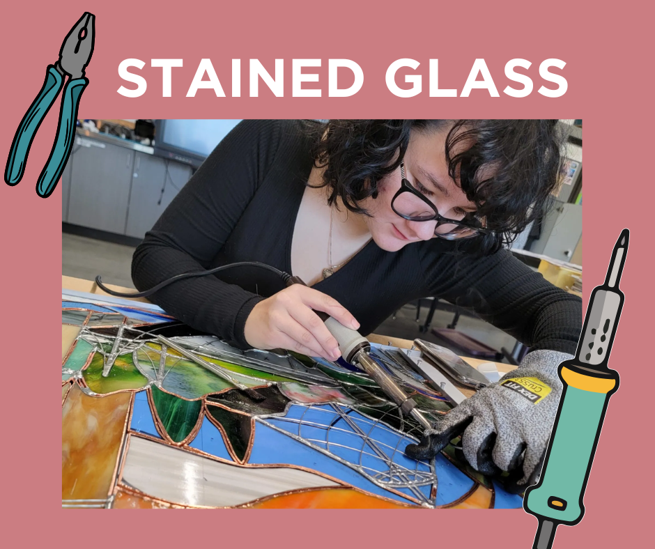 A woman working on creating a stained glass art piece using a soldering iron in a workshop.