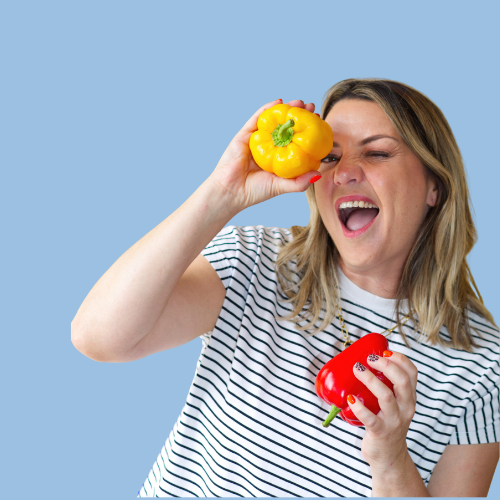 Woman holding yellow and red bell peppers, smiling and playing with one near her eye.