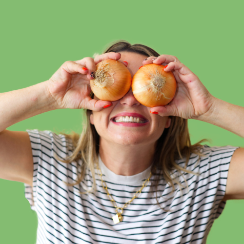 Woman holding two onions in front of her eyes against a green background.