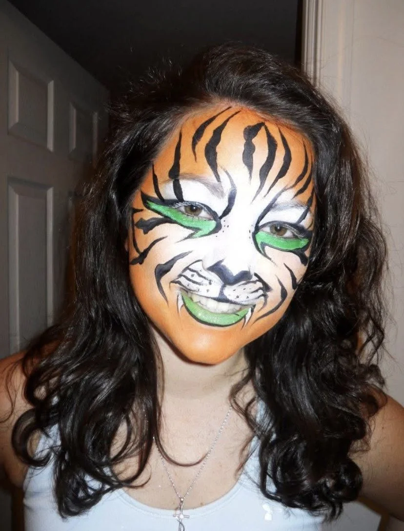 Woman with tiger face paint featuring orange, black, white, and green colors.