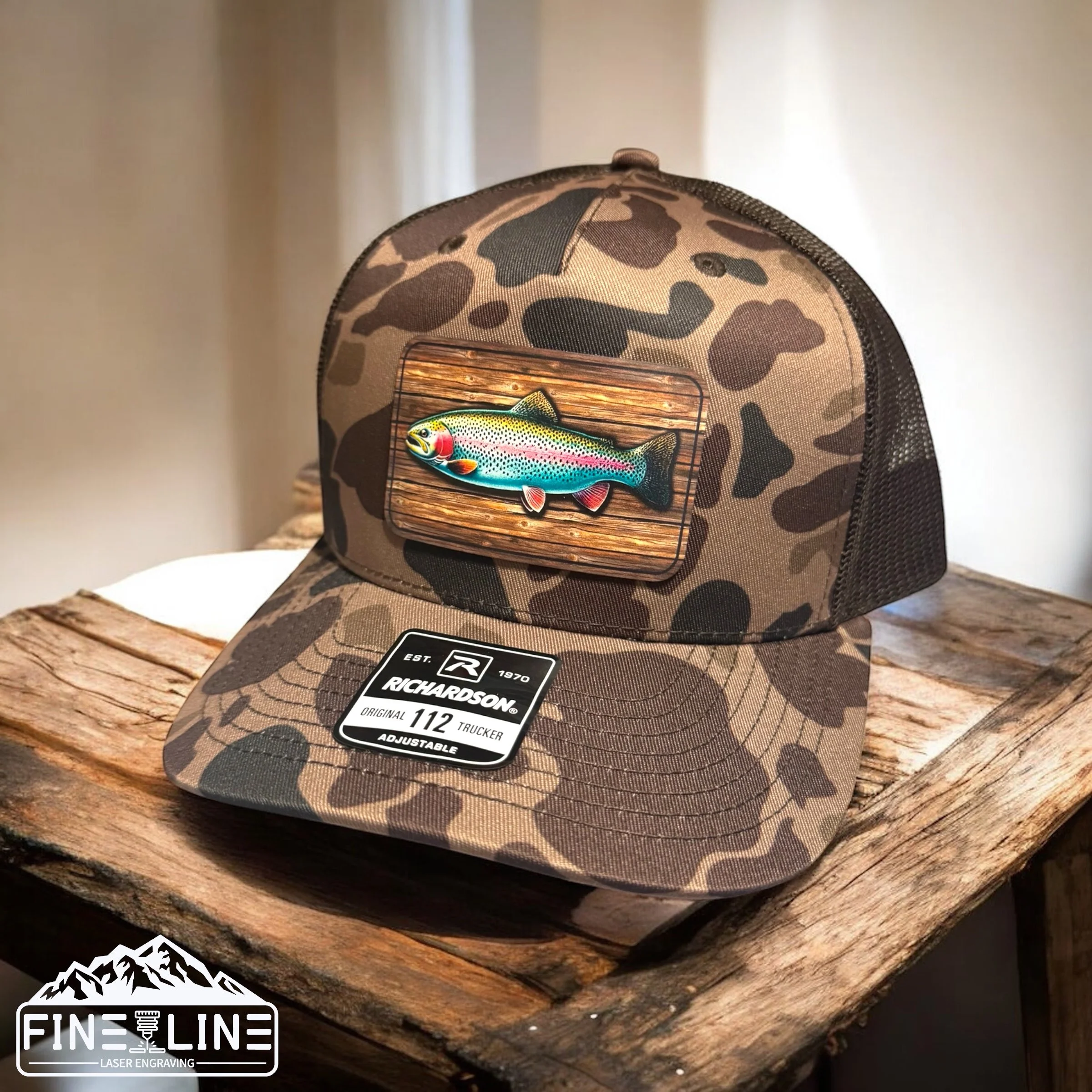 Camouflage trucker hat with colorful fish patch, resting on a rustic wooden surface.