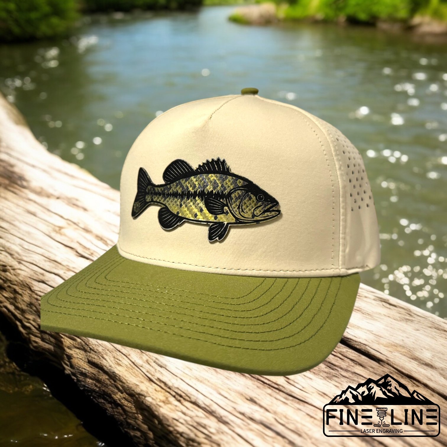 A trucker cap with a green brim and white front, featuring a fish patch on the front, placed on a piece of wood near a river with greenery in the background.