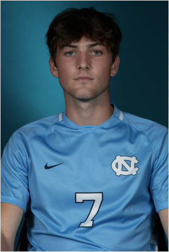 Young man with brown hair wearing a light blue sports jersey with the number 7 and a logo of a Carolina blue football team.