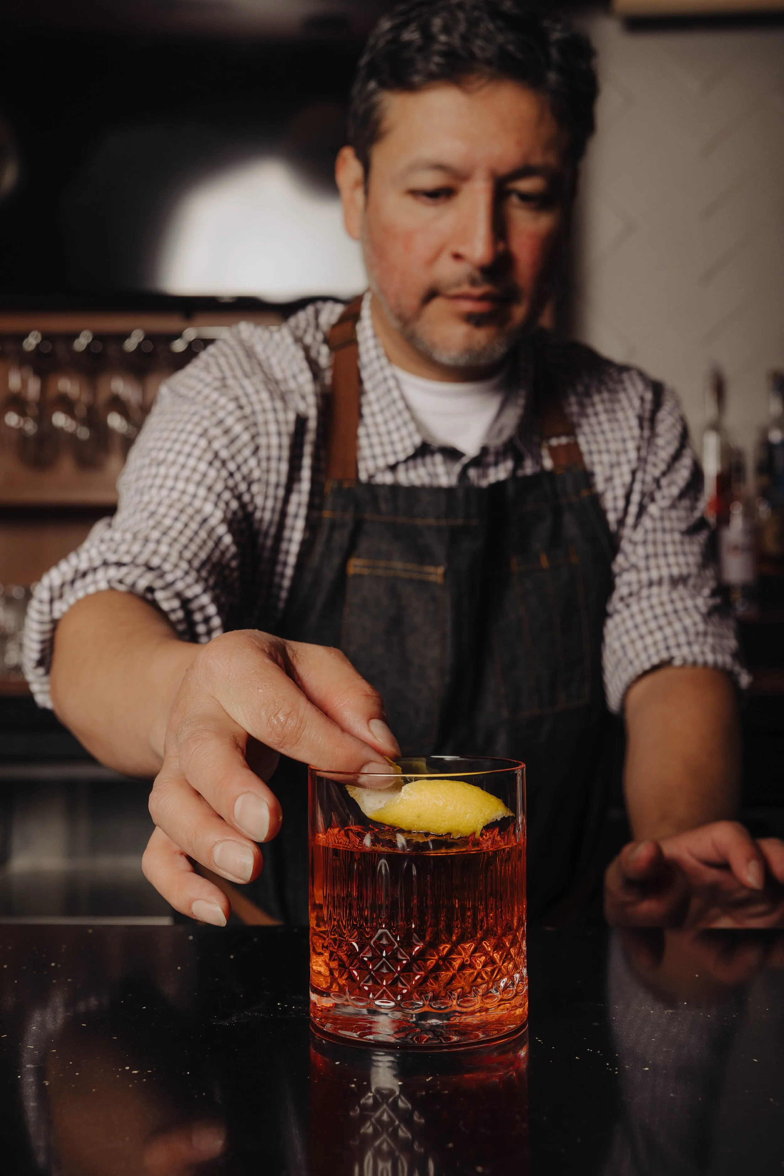 A bartender garnishing a cocktail with a lemon twist in a dimly lit bar.