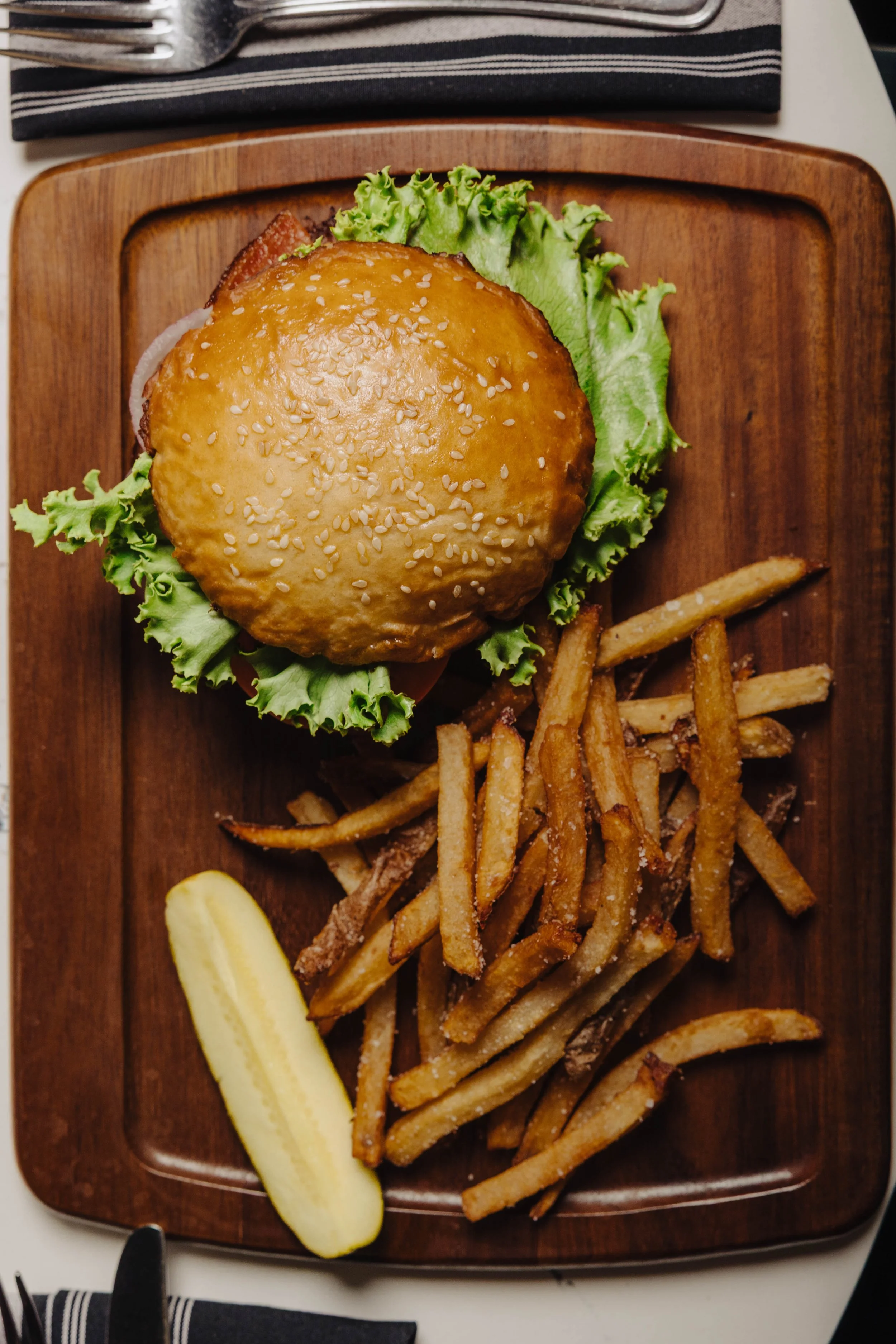 Cheeseburger served with French fries and a pickle spear on a wooden serving board.